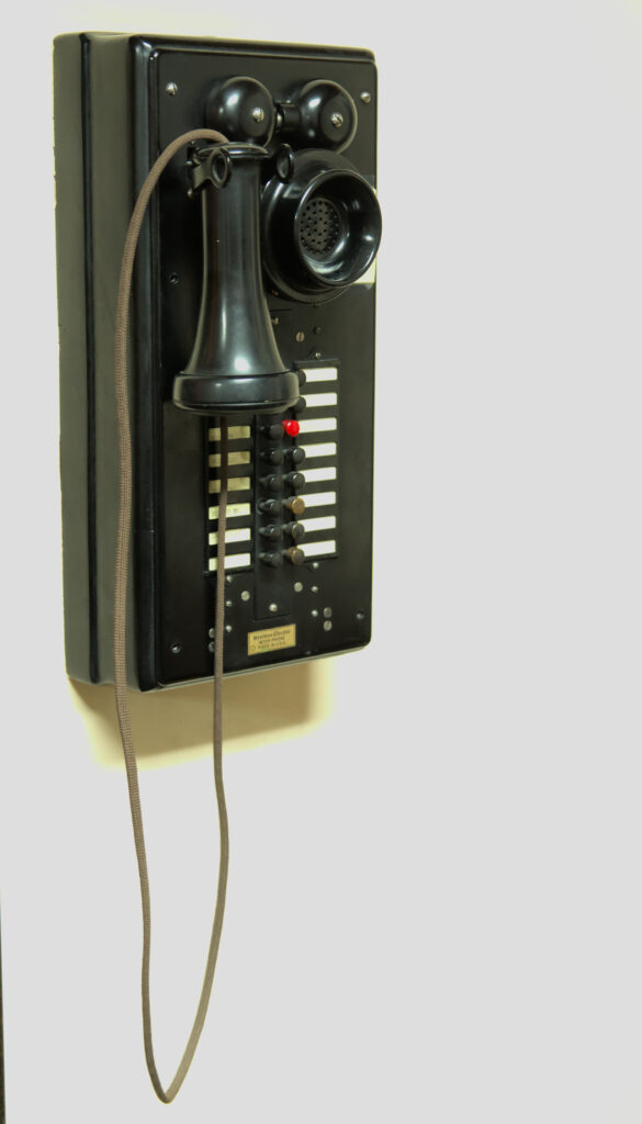 On old style wall phone. Detachable mouth speaker, with ear speaker on the body of the phone. A bright red button is the only thing of color on this phone.
